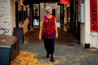 Photo of a woman walking through a laneway in Salamanca, Hobart. She is warmly dressed in with a bright orange longsleeve shirt complimented with a handmade wool dress in red and purple from the Salamanca Woolstore.. 