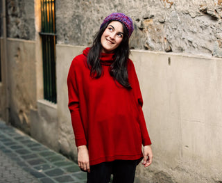 Woman wearing beautiful red merino jumper and pink and purple beanie from the Salamanca Wool Shop. The woman is looking happy and standing in a laneway in Salamanca, Tasmania.